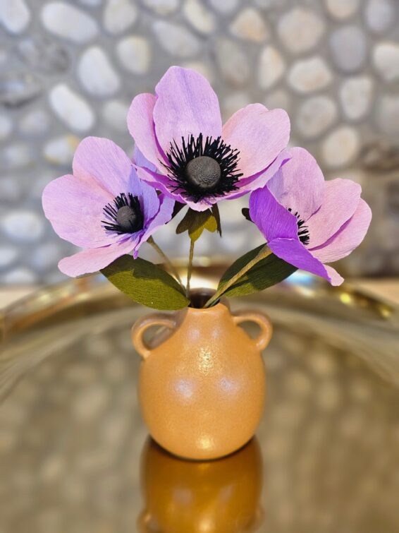 Lila papieren anemonen in een abrikooskleurig kruikje.