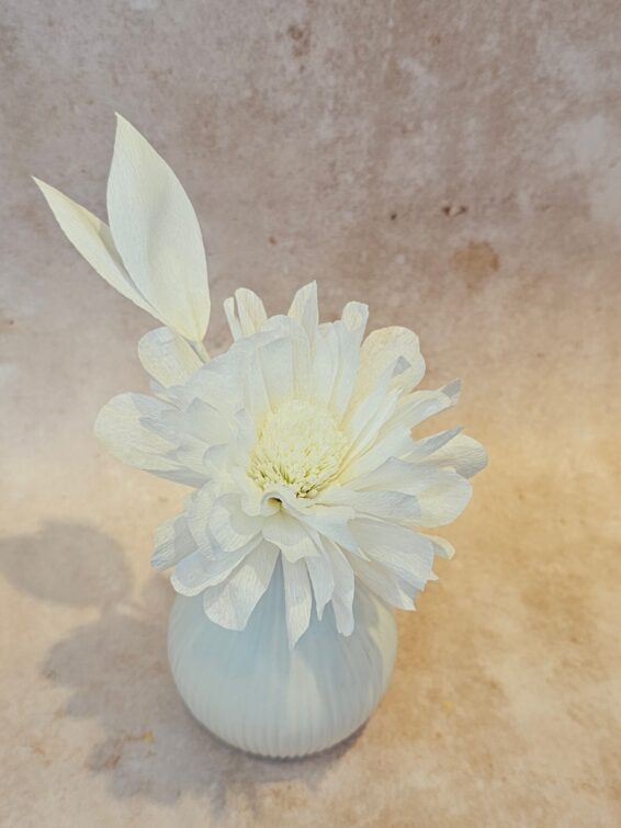 Een roomwitte papieren bloem in een licht knopvaasje.