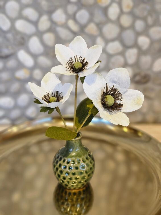 Witte papieren anemonen in een groen knopvaasje.